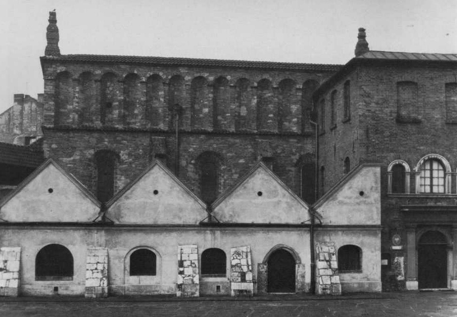 Photographie en noir et blanc d'un grand bâtiment en briques avec plusieurs toits pointus à pignon, identifié comme une synagogue historique.