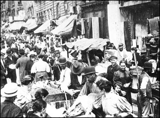 Photographie ancienne d'une rue marchande animée du Lower East Side new-yorkais, étals et passants en foule.