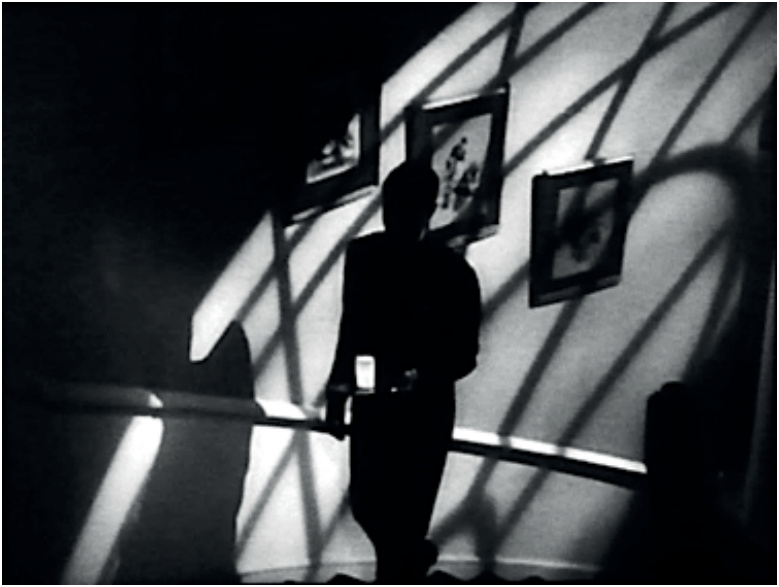 Photogramme en noir et blanc : Cary Grant en costume sombre, gravissant un escalier en tenant un verre de lait lumineux dans *Suspicion*.